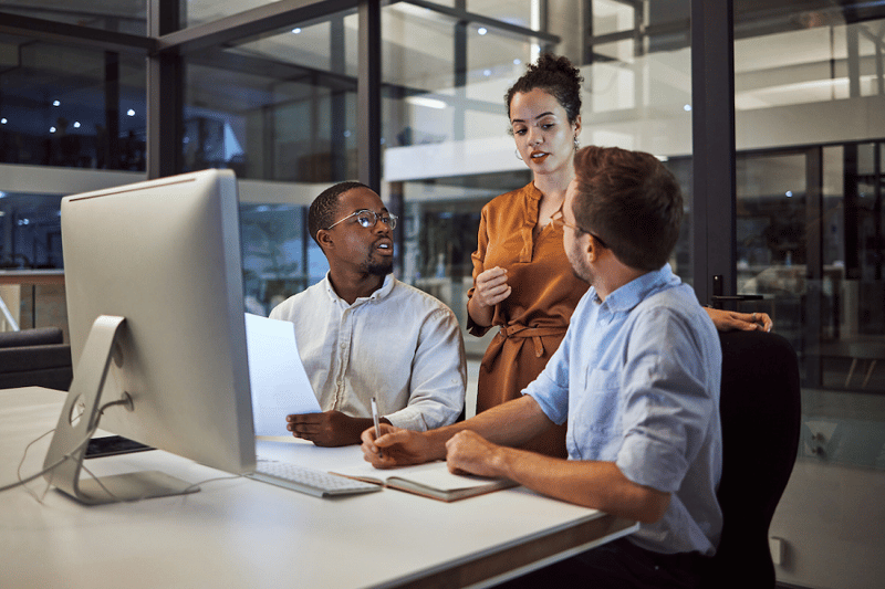 Three coworkers talking in front of a computer