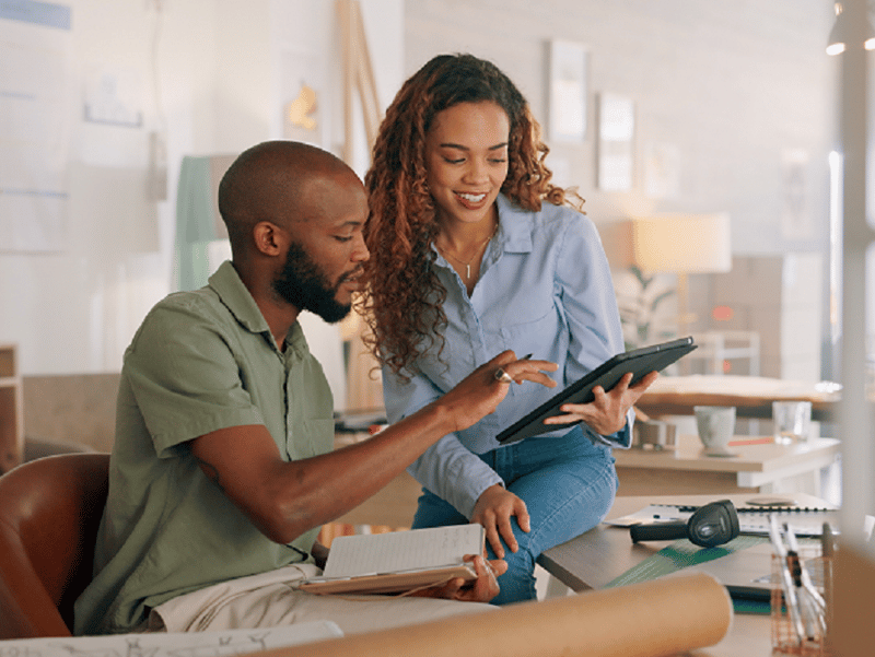 Two smiling people looking at a tablet, one is reaching over to show the other something