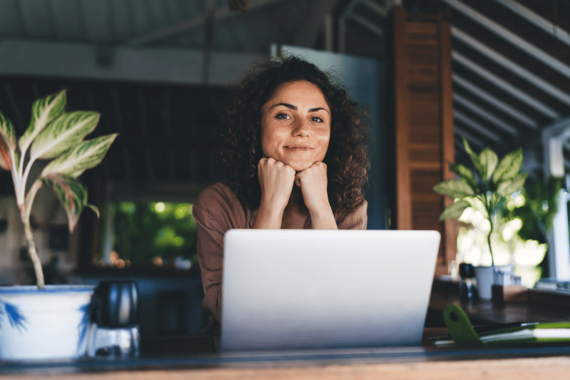 Slightly smiling woman with curly hair looking at camera, with laptop in front of her