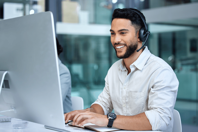 Smiling man wearing grey shirt and headset looking at his computer